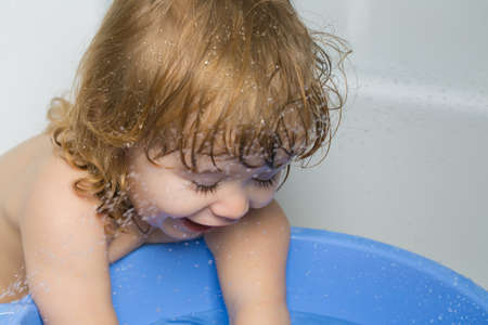 Small cute funny baby boy with blonde wet hair in bath water