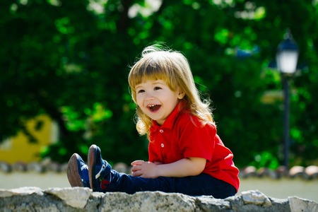 Cute laughing little boy with long hair on the stone fenceの写真素材
