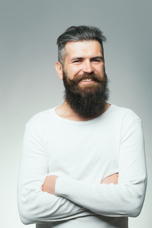 handsome young man with long dark haired beard and smiling face in white shirt on grey background