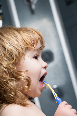 Small cute funny baby boy with blonde wet hair in bath cleaninng teeth with brushの写真素材