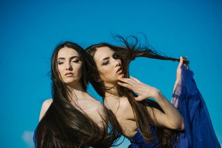 young pretty women with long windy hair in elegant violet dresses sunny day outdoor on blue sky backgroundの写真素材