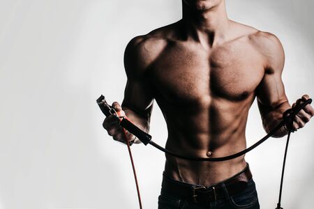 Sexy muscular male torso of athlete bodybuilder posing in power with veins on hands and bare chest holding rope on white backgroundの写真素材