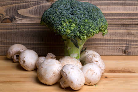 Fresh champignons unpeeled white button mushrooms and broccoli on wooden backgroundの写真素材