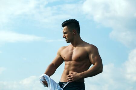 young macho man model athlete with muscular body and wet bare chest outdoor on sky background...