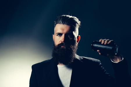 Handsome young man with long beard and moustache in black jacket holding tin beer can bottle in studio on grey backgroundの写真素材