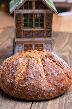 Round loaf of homemade bread and small house model on wooden backgroundの写真素材