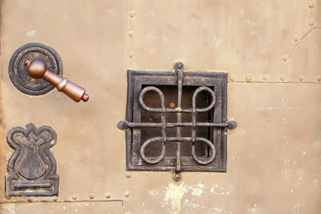 Small square wrought iron grating window and doorknob on metal armor texture background closeupの写真素材