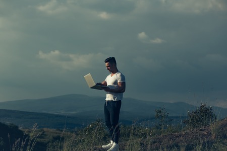 Young handsome man with muscular sexy body standing with laptop outdoor sunny day on blue sky backgroundの写真素材
