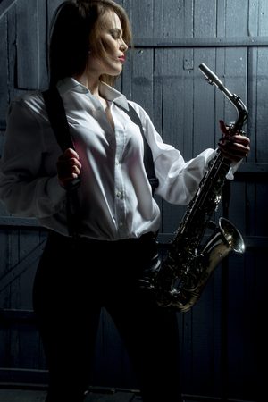 young pretty woman with sexy stylish cloth playing saxophone in retro braces and pants with shirtの写真素材