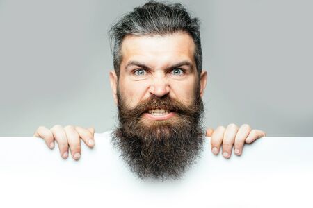handsome bearded man with long lush beard and moustache on evil face with white paper sheet in studio on grey background, copy spaceの写真素材
