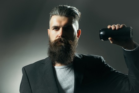 Handsome young man with long beard and moustache in black jacket holding tin beer can bottle in studio on grey backgroundの写真素材