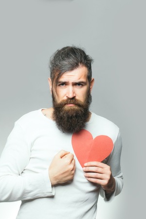 young bearded man with sad face holding red paper heart in studio on grey background, copy spaceの写真素材