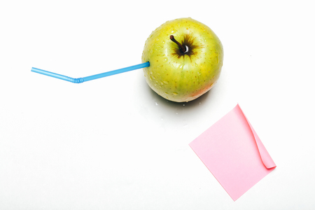 Fresh green apple with water drops and blue drinking straw inside making juice isolated on white background with pink paper sheet - healthy food and drink concept, copy spaceの写真素材