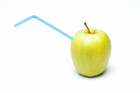Fresh green apple with water drops and blue drinking straw inside making juice isolated on white background - healthy food and drink concept, copy spaceの写真素材