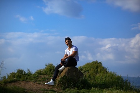 Young sexy man with muscular sexy body sitting outdoor with water bottle on sky natural background