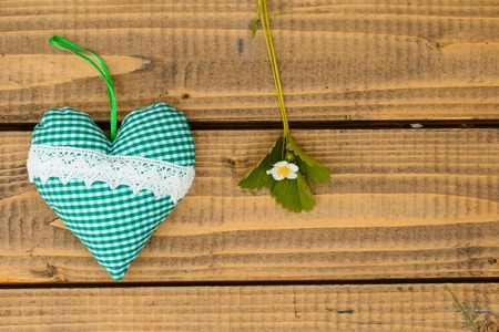 strawberry blossom and green leaves branch on brown textured wooden background with small aroma pillow in heart shapeの写真素材