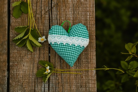 strawberry blossom and green leaves branch on brown textured wooden background with small aroma pillow in heart shapeの写真素材