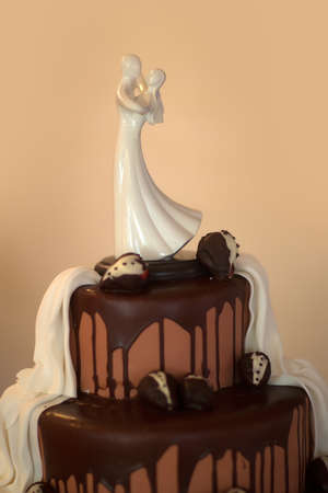Wedding cake with bride and groom porcelain figurine topper on beige background