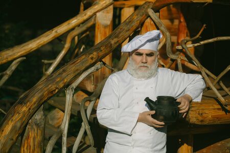 bearded man cook chef in uniform and hat with long beard on serious face holding iron old tea kettle...