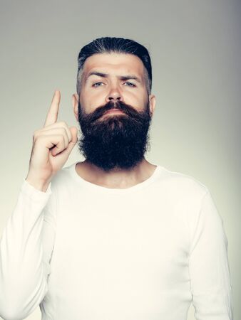 handsome young man with long beard and moustache on face with raised finger on grey background in studioの写真素材
