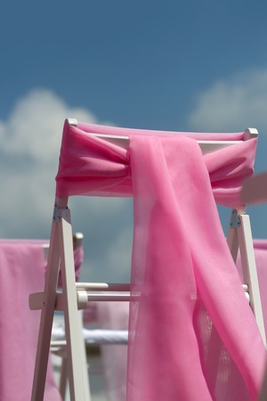 Pink bows ribbon decoration on white wedding chairs on blue sky backgroundの写真素材