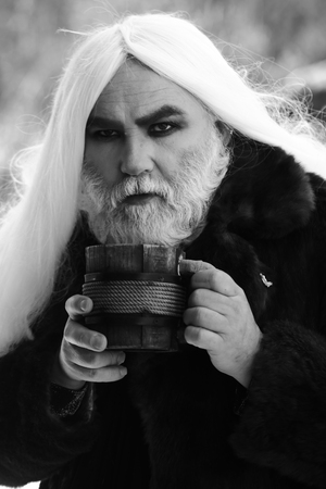 Druid old man with long silver hair and beard in fur coat with wooden mug in hands black and white...