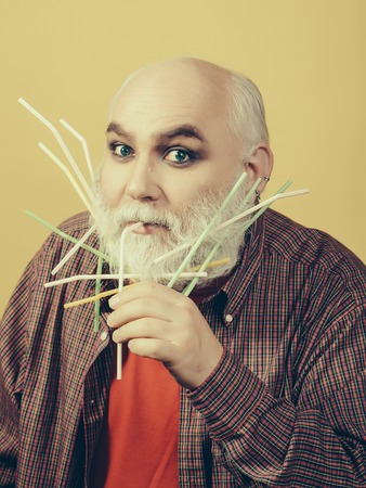 Old bearded man with many drinking straws in long grey beard on surprised face in red checkered...