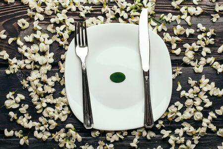 Plate with fork and knife in white acacia blossoming flower petals decorative frame on dark wooden...