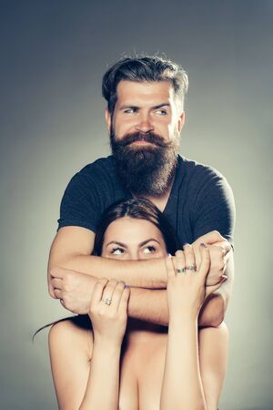 Handsome bearded man with smiling face embracing young woman topless in studio on grey backgroundの写真素材