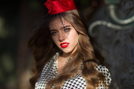 Sexy woman brunette long hair poses in red garrison cap with black veil on sunny day on dark...