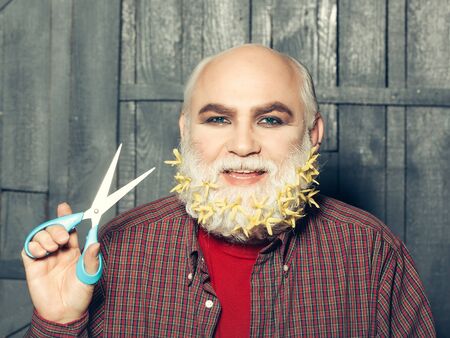 old bearded man with yellow flowers in long grey beard on smiling happy face in red checkered shirt...
