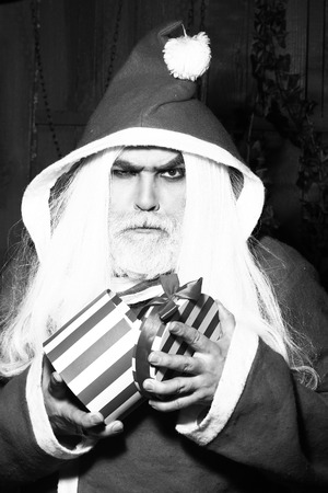 New year man with serious face with long beard and hair in santa claus christmas coat holding present box, black and whiteの写真素材