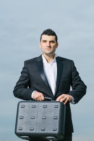 handsome male businessman with serious face in black formal jacket and white shirt with brief case...
