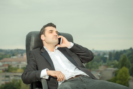 handsome male businessman with serious face in black formal jacket and white shirt speaking on...