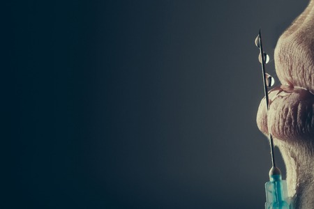 young woman holding with hand syringe with liquid drop near sexy lips and mouth on grey backgroundの写真素材