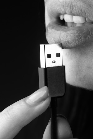female mouth with sexy lips holding with finger usb flash wire cable for connection, closeup, black and whiteの写真素材