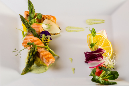 Grilled salmon steaks garnished with sauce lemon flower asparagus and vegetables on white backgroundの写真素材