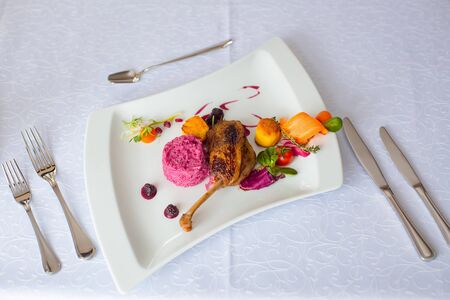 Confit duck or goose leg crisp delicious served with garnish red tomatoes vegetables and blackberry sauce on white backgroundの写真素材
