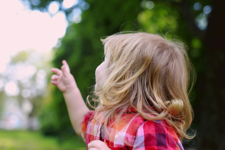 small boy child with happy face and long blonde hair in checkered red shirt on fresh green natural background outdoorの写真素材