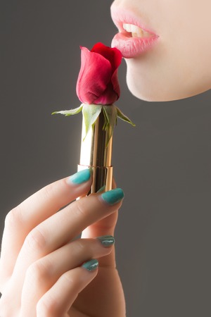 female hands with tender skin and blue manicure holding rose flower with soft petals red color in lipstick near sexy lipsの写真素材
