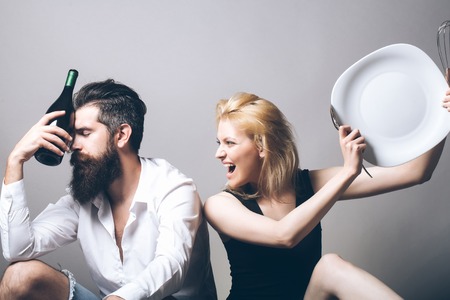 young family couple in quarrel of blonde pretty girl with kitchen utensils and bearded man with long beard holding wine bottle sitting on bathtub. household, everyday life and routineの写真素材