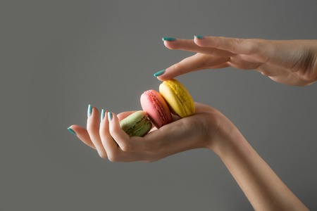 female hands with soft tender skin and blue manicure holding colorful french biscuits of macaron or...