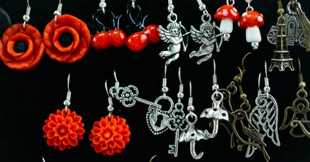 many small fashion female earrings red and silver colors on black fabric background sales in bazarの写真素材
