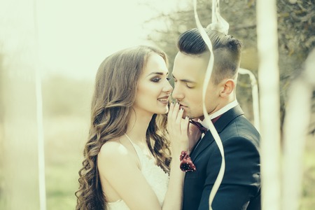 Happy newlywed couple posing and smiling in wedding dress and suit in forest decorated with ribbons outdoorの写真素材