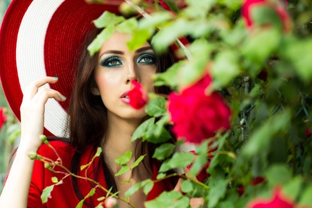 young glamour woman with bright makeup on pretty face in red round retro hat with rose flowers outdoor, closeupの写真素材