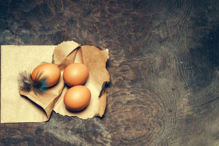 Domestic eggs decorated with beautiful feather on pack brown paper on dark wooden background closeup...