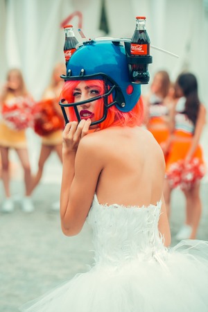Ukraine, Kyiv - July 27, 2016: young patriotic sexy woman with pretty face and orange hair in soccer drink helmet with coca cola bottles and american flag celebrating independence day usaのeditorial素材