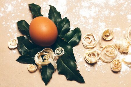Brown egg on green laurel leaf and excelsior on pack paper background decorated with white flour...