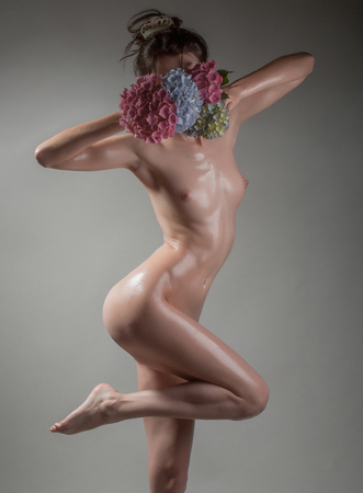 young pretty woman with naked sexy slim wet body and naked chest with belly holding hydrangea flower bouquet in hands on studio grey backgroundの写真素材