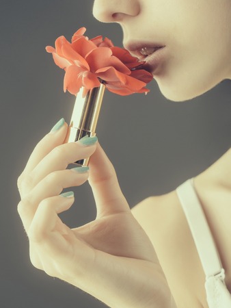 female hands with tender skin and blue manicure holding rose flower with soft petals red color in lipstick near sexy lipsの写真素材